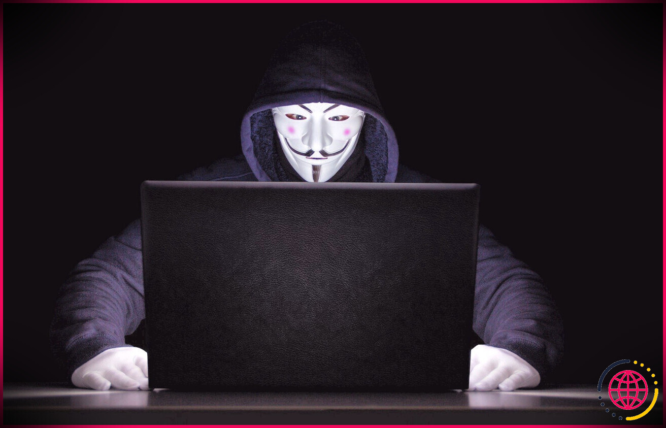 Personne portant un masque anonyme assis devant l'ordinateur 