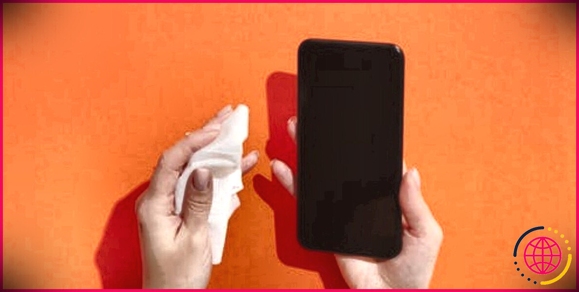 mains tenant un tissu et un smartphone noir sur fond orange