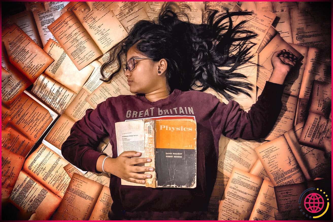 Un étudiant endormi avec un manuel de physique sur une pile de pages