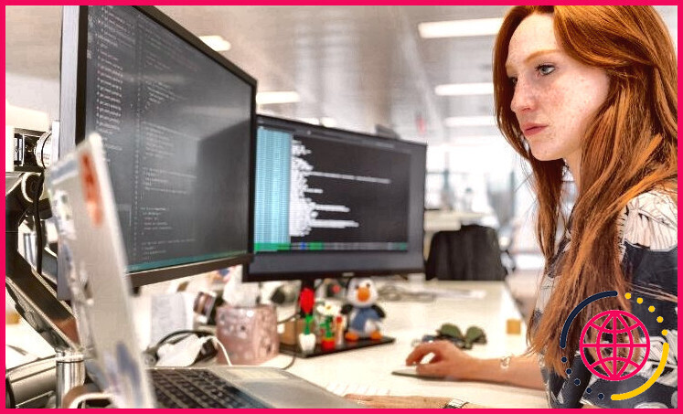 femme aux cheveux rouges travaillant sur deux écrans d'ordinateur et un ordinateur portable à un bureau