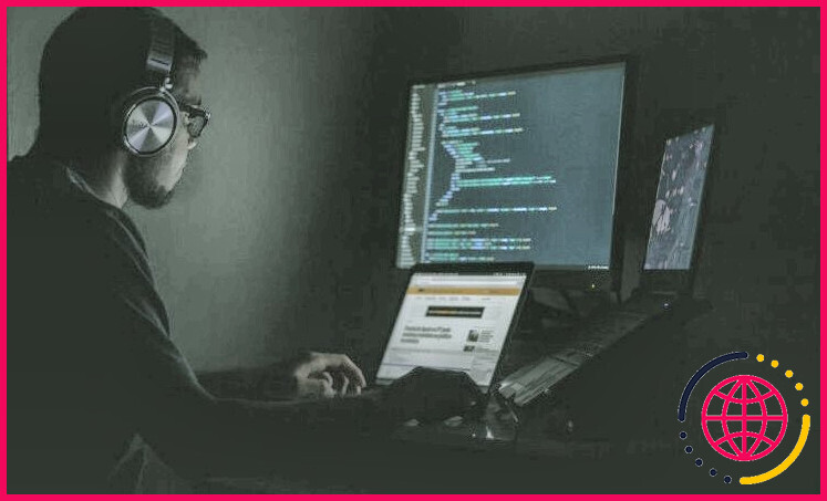 homme avec un casque assis dans une pièce sombre éclairée par un écran d'ordinateur avec codage