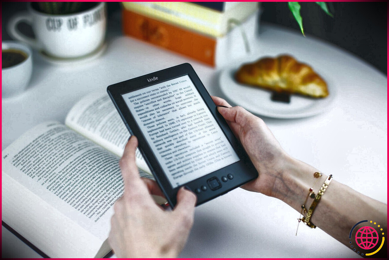 Deux mains tenant un Kindle avec un livre physique en arrière-plan